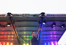 Brie Treviranus striking a pose on stage with the stage lights set to the pride rainbow.