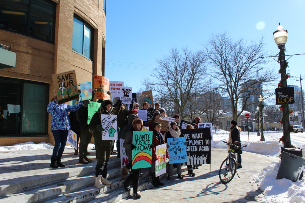 Protestors stand on the stairs in front of Waterloo City Hall holding signs demanding climate action.