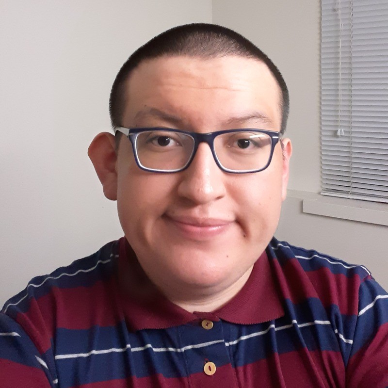 A person wearing glasses and a striped polo shirt, possibly a UW student, is smiling and looking at the camera. The background features a window with blinds and a white wall.