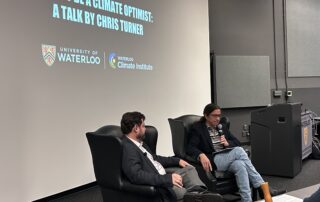 Two people sit in armchairs on a stage, engaging in a discussion. A projection behind them reads "How to Be a Climate Optimist: Solutions and Insights by Chris Turner," with logos for the University of Waterloo and Waterloo Climate Institute.