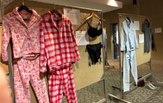 A vibrant display of colorful pajamas and clothing on racks evokes the creativity of an art exhibit. The left rack features patterned pajama sets, while the right showcases garments including a blue pajama set and a striped outfit, all against the backdrop of a neutral-colored wall.