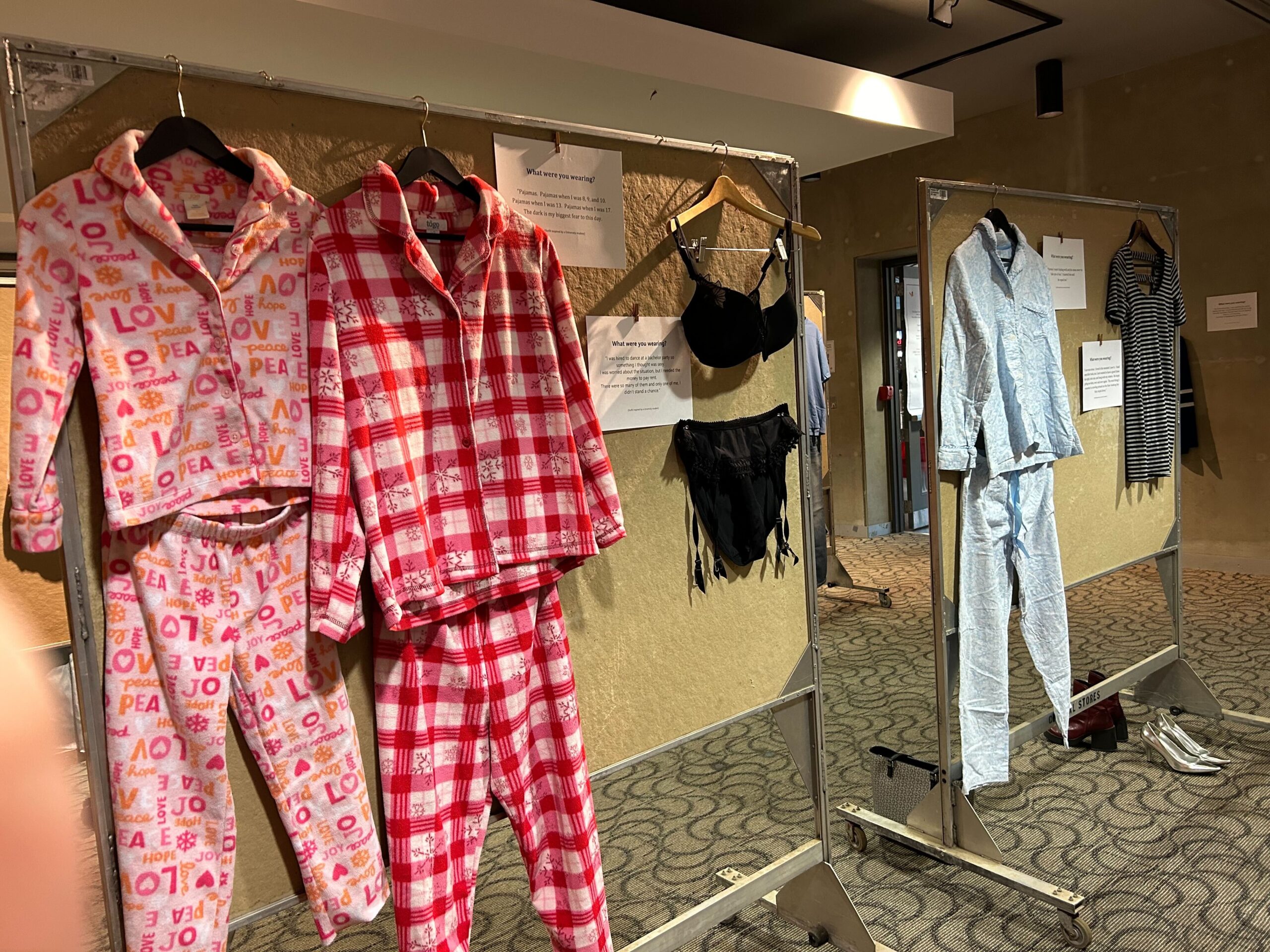 A vibrant display of colorful pajamas and clothing on racks evokes the creativity of an art exhibit. The left rack features patterned pajama sets, while the right showcases garments including a blue pajama set and a striped outfit, all against the backdrop of a neutral-colored wall.