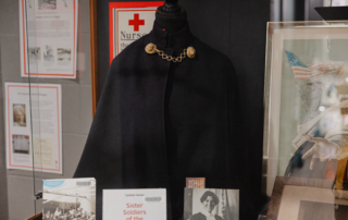 A display case showcasing a historical nurse's cape with gold details, several books, and framed photos commemorates the pivotal role of wartime nurses. The items reflect on nurses' contributions in wars, a fitting tribute for Remembrance Day at St. Jerome’s University.