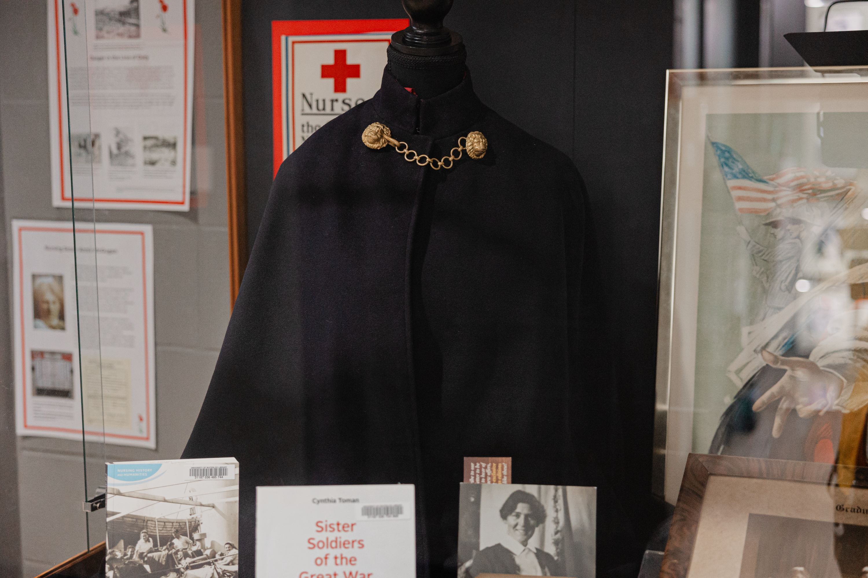 A display case showcasing a historical nurse's cape with gold details, several books, and framed photos commemorates the pivotal role of wartime nurses. The items reflect on nurses' contributions in wars, a fitting tribute for Remembrance Day at St. Jerome’s University.