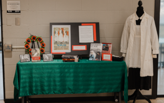 A table draped in green at St. Jerome’s University showcases a framed poster, books, photos, and wartime memorabilia. Highlighting the role of wartime nurses, a mannequin dons a vintage nurse uniform. A wreath for Remembrance Day and informational text complete the display.