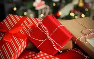 A pile of wrapped gifts featuring red, striped, and brown paper, each adorned with red and white twine, looks enchanting. Blurred lights and festive decorations hint at a holiday setting, as if each present holds joy rather than an unexpected parking ticket.