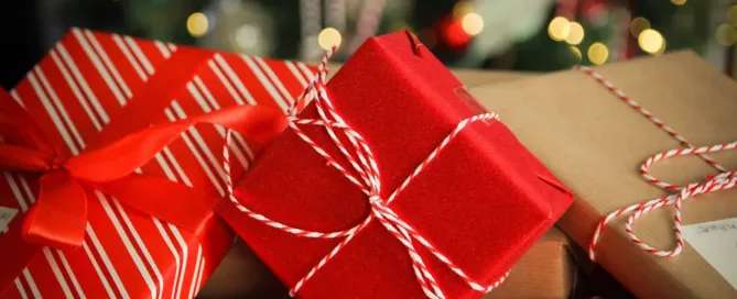 A pile of wrapped gifts featuring red, striped, and brown paper, each adorned with red and white twine, looks enchanting. Blurred lights and festive decorations hint at a holiday setting, as if each present holds joy rather than an unexpected parking ticket.