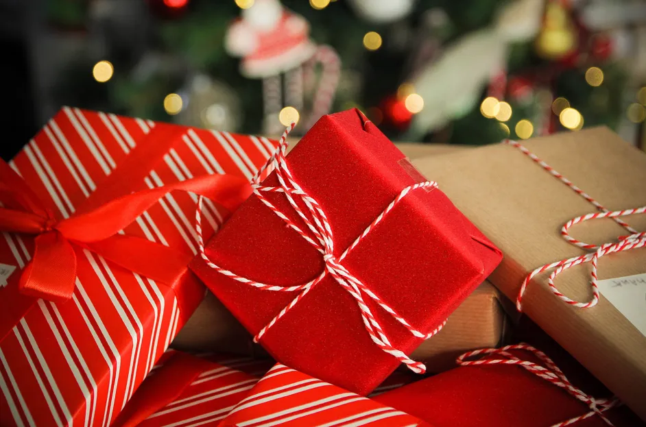 A pile of wrapped gifts featuring red, striped, and brown paper, each adorned with red and white twine, looks enchanting. Blurred lights and festive decorations hint at a holiday setting, as if each present holds joy rather than an unexpected parking ticket. 