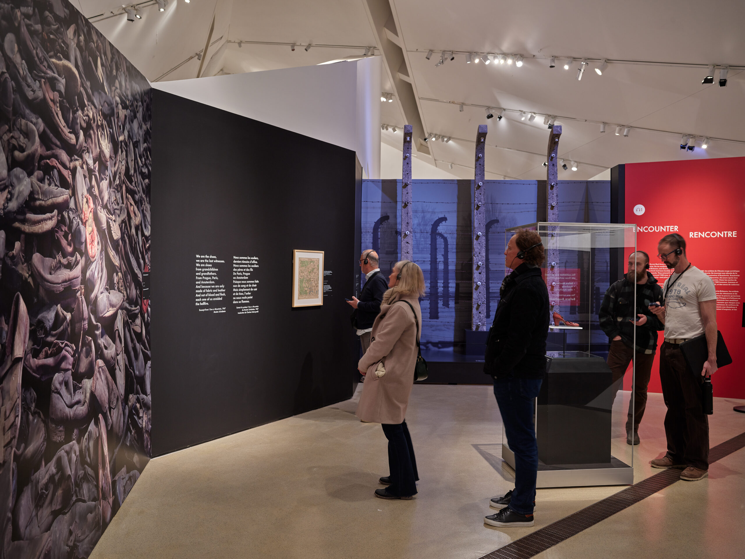 Visitors in a museum hall observe a large artwork depicting intertwined figures. The ROM exhibit features text panels and informational displays, while modern lighting illuminates the room with more exhibits in the background.