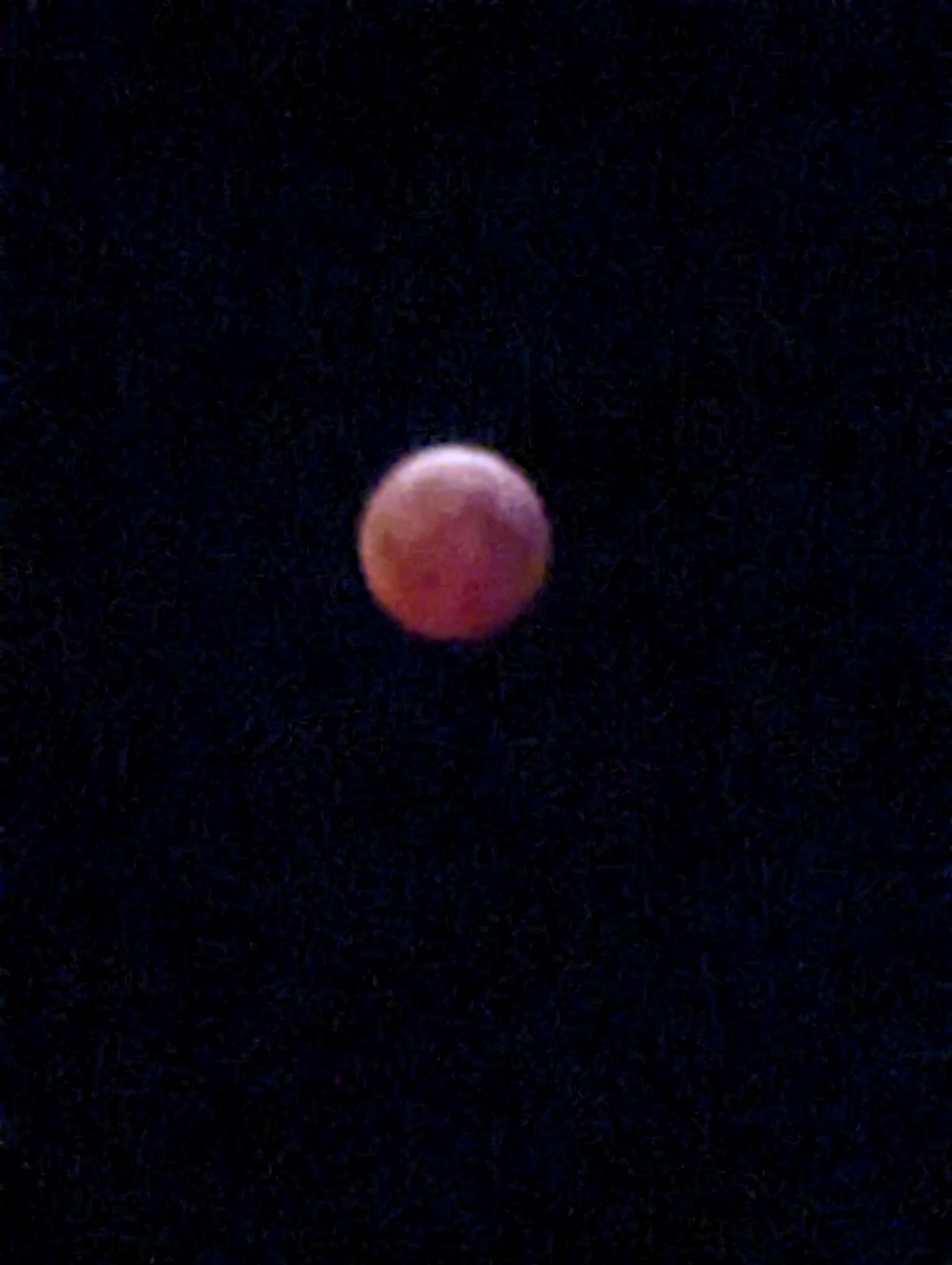 A red moon glows vividly in the night, casting a reddish hue that's iconic of a total lunar eclipse.