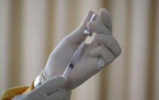 A gloved hand holds a vaccine vial and syringe, drawing liquid from the vial against a blurred, neutral background—highlighting the importance of measles vaccination in protecting public health.