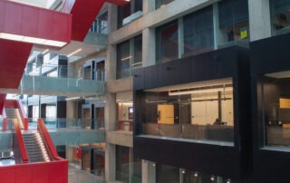 A modern building interior on the UW campus with large glass windows, concrete walls, red staircases, and suspended walkways connecting multiple floors—an open, spacious design ideal for a student advocacy group’s activities.