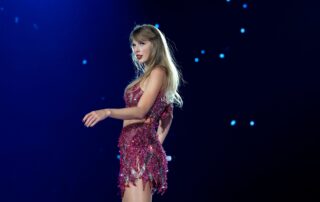 A woman with long blonde hair wearing a sparkly pink dress performs on stage under blue lighting, small lights behind her resembling stars—a captivating scene straight from The Life of a Showgirl.