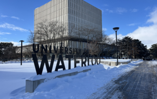 A large "University of Waterloo" sign stands before a modern concrete building on a snowy campus under a blue sky, capturing the scene without a hint of the disappointing experience or negative review one might find in customer feedback elsewhere.