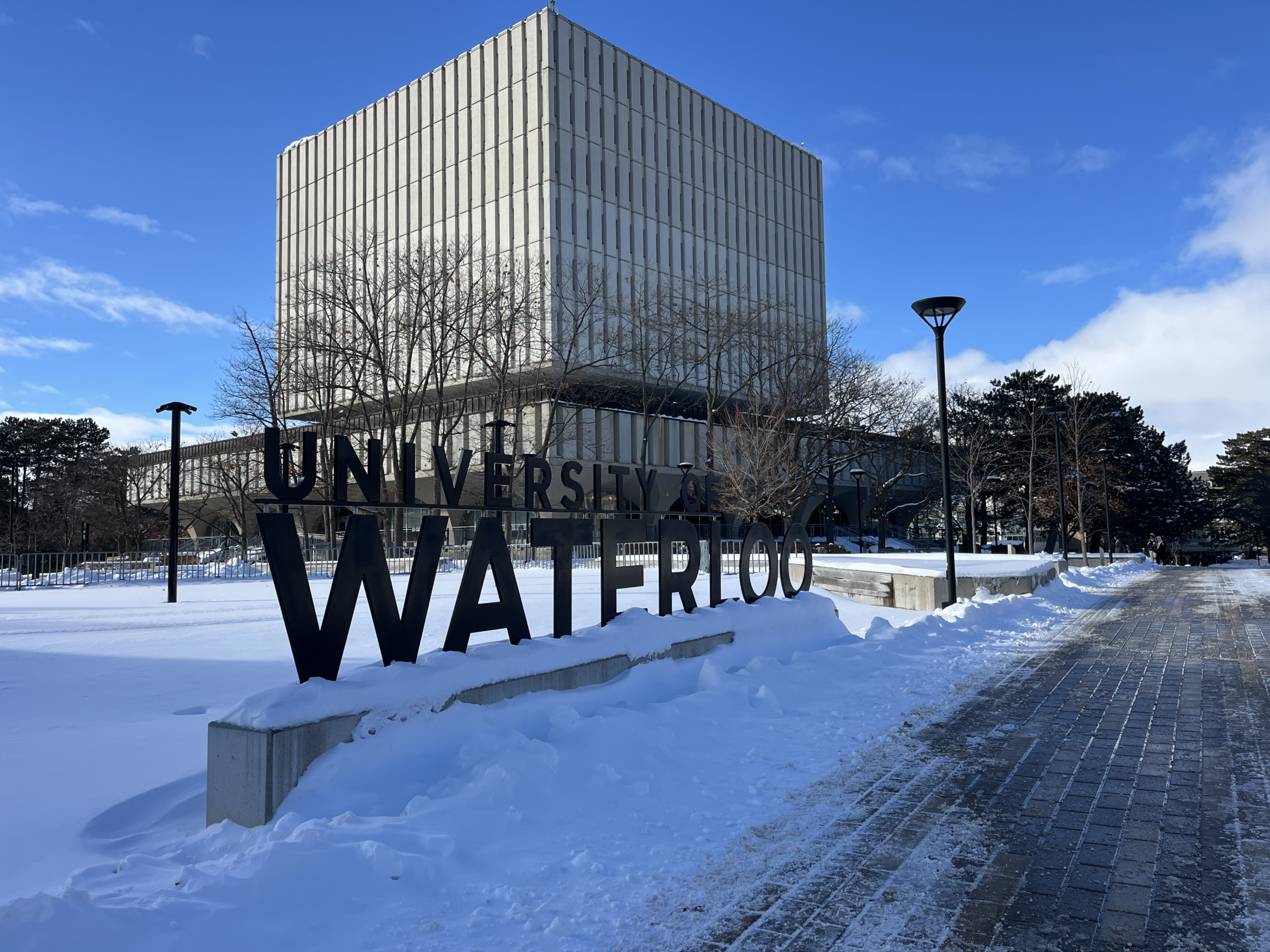 A large "University of Waterloo" sign stands before a modern concrete building on a snowy campus under a blue sky, capturing the scene without a hint of the disappointing experience or negative review one might find in customer feedback elsewhere.